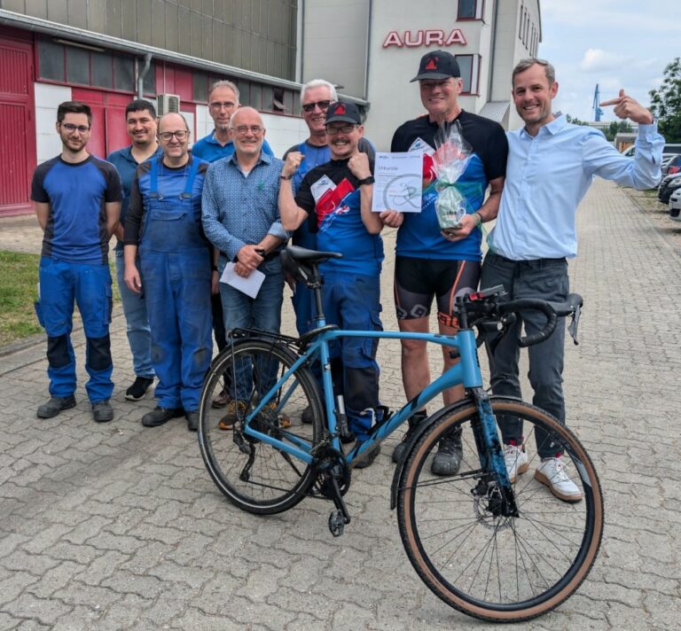 9 Personen vor dem Hauptgebäude mit einem Fahrrad